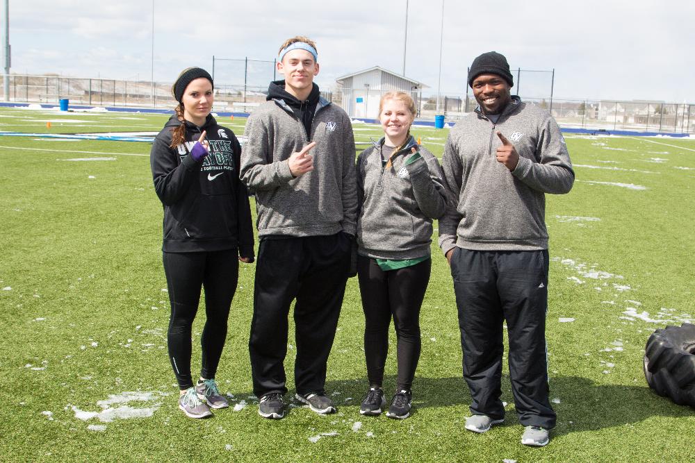 Four Staff members on the soccer field hold up the number 1